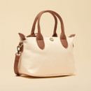 Cream mini cross-body bag shown at an angle, featuring tan top handles, a zip closure and gold-tone hardware.