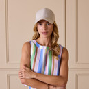 Woman wearing a beige linen baseball cap styled with a multicoloured striped sleeveless top.