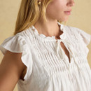 Close-up side view of a woman wearing a white sleeveless blouse with ruffled cap sleeves and fine smocking across the chest.