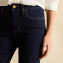Close-up of the front waist and pockets of dark-wash skinny jeans, featuring contrast stitching and a gold button.