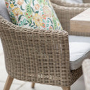 Detail of a woven rattan-effect dining chair with a light coloured seat cushion and a floral patterned scatter cushion.