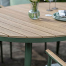 Detail of a round slatted wood effect garden table top with a green metal rim, styled with plates and a small vase of flowers.