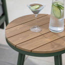 Round wood-effect slatted side table with sage green frame, styled with a drink glass and a water jug.