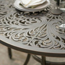 Close-up of the bronze round metal tabletop showing the decorative cut-out pattern, with tableware and a glass visible at the edge.