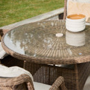 Close-up of the round glass-topped wicker dining table showing the woven pattern beneath the glass and stacked ceramic bowls placed at the edge