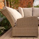Close-up side view of a beige rattan outdoor sofa showing curved arm detailing and thick cushioned back support.