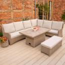 Rattan garden corner sofa and height-adjustable table with beige cushions on a wooden patio, decorated with fruit and drinks.
