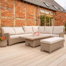 Curved rattan outdoor sofa with beige cushions paired with a rectangular rising table and bench-style seat on a garden deck.