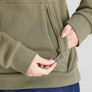 Close-up detail of the khaki green hoodie’s front pocket, highlighting the vertical zip compartment and ribbed hem. The model’s hand is holding the zipper pull.