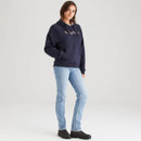 Full-length view of a woman wearing a navy blue hoodie styled with light blue straight-leg jeans and black ankle boots. The hoodie has ribbed cuffs and hem, a front kangaroo pocket, and chest logo text, photographed against a neutral grey studio background.