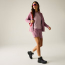 Full-length view of a model wearing the pink textured zip-up jacket open over a pink top, with matching shorts, hiking boots and sunglasses.