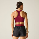 Rear view of a model wearing a burgundy racerback sports bra with ventilated mesh panel and black running shorts.