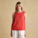 Woman wearing a sleeveless red linen top paired with white trousers, shown against a neutral beige backdrop.