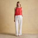 Full-length look of a woman wearing a sleeveless red linen top with wide-leg white trousers, posed against a neutral background.