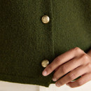 Detail of gold embossed buttons on an olive green knitted vest, showing the textured finish of the fabric.