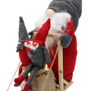 Close-up of two small gonks sitting on a lit hessian sack in front of the large gonk on the wooden sledge, on a white background.