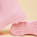 Close-up of light-pink rain boots, showing the textured outsole, ribbed heel, and smooth, waterproof upper.