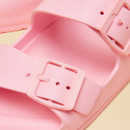 Close-up of a light pink sandal showing the textured buckle and smooth upper strap detail.