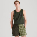 Man wearing a dark green Ridgeline vest with contrast olive trim, paired with two-tone green shorts featuring a solid panel and pixelated houndstooth print, standing against a plain light background.