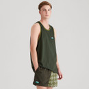 A model standing in a dark green Ridgeline sleeveless singlet with logo patch on the chest, styled with green two-tone shorts that feature a bold houndstooth-like pattern.