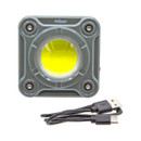 A square, grey LED work light with a circular, yellow bulb in the centre and four screws at the corners. A black USB charging cable is placed below.