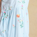 Fabric close-up of a light blue and white striped dress with soft floral motifs in pink, yellow and green.