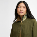 Close-up of the model’s face and upper jacket, highlighting the raised collar with tartan detail and the gold ring zip pull.