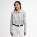 Model wearing a Barbour women’s long-sleeve checked shirt in cream with navy and pale green lines, styled with white jeans and a brown belt.