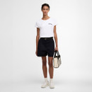 Full-length view of the model in the white Barbour T-shirt and black shorts, holding a tote bag and wearing trainers.