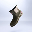 Angled studio shot of an olive green Barbour women’s ankle wellington boot featuring elastic side panel, textured rubber finish and pink heel detail against a pale gradient background.