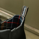 Close-up of the interior of a black Barbour Chelsea wellington boot showing tartan lining and branded fabric pull tab.