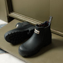 Black Barbour Chelsea wellington boots with chunky lug sole, shown on a doorstep with a matte rubber finish and pull tab at the heel.