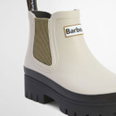 Close-up of a cream Barbour Chelsea boot showing the elastic side panel, branded logo patch, smooth waterproof rubber upper and chunky black lug sole.