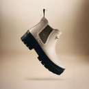 Cream Barbour Chelsea boot shown in mid-air with water droplets, highlighting waterproof construction and rugged sole.