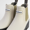 Close-up of cream Barbour Chelsea boots showing logo patch, elastic side gusset and smooth waterproof upper.