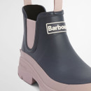Angled front view of a Barbour navy Chelsea wellington boot with blush pink sole and smooth waterproof upper.