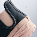 Detail shot of a Barbour navy Chelsea wellington boot with water droplets on the waterproof upper and textured blush pink sole.