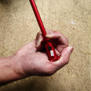 A hand grips a red metal rod with a cylindrical base labelled "4680" against a textured, brown surface. The image conveys focus and precision.