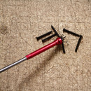 A red magnetic pickup tool lifts several black screws against a textured beige background. The tool and screws suggest a workspace or DIY setting.