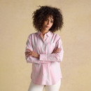 Woman wearing a pink long-sleeve striped button-down shirt with green and white vertical stripes, styled with cream trousers against a neutral studio background.