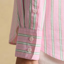 Detailed view of the shirt cuff with white buttons and green and white vertical stripe pattern on pink fabric.