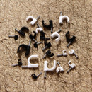 A scattered collection of black and white plastic cable clips with silver nails on a textured brown wooden surface, conveying a sense of organization.