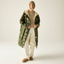 Full-length view of a model wearing a long khaki-green changing robe with cream horse print, cream lining, beige knit jumper and off-white jeans.