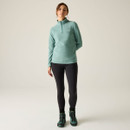 Full-length view of the model wearing the ivy green half-zip fleece with black leggings and teal hiking boots.