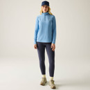 Full-length view of a model wearing a washed denim blue women’s half-zip fleece with a high collar.