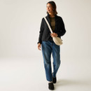 Full-length view of model wearing a black full-zip fleece jacket with a high collar, blue jeans and a cream crossbody bag.