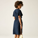 Back view of a woman wearing a navy midi dress with short sleeves and a drawstring waist, holding a straw tote bag.