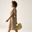 Side view of a woman wearing a leopard print dress with short sleeves and a drawstring waist, carrying a straw handbag.