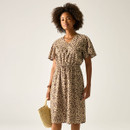 Woman wearing a leopard print V-neck dress with short sleeves and a drawstring waist, holding a straw handbag.