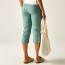 Rear view of green cropped trousers showing back pockets and cropped length, with model holding a cream tote bag and wearing beige clogs.